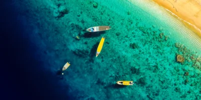 Luchtfoto van boten in turquoise kustwater naast een zandstrand