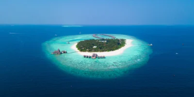 Luchtfoto van een bebost eiland met wit strand en turquoise lagune op de Malediven