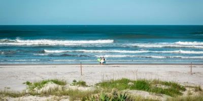 Twee mensen met surfplanken op New Smyrna Beach, met brekende golven op de achtergrond