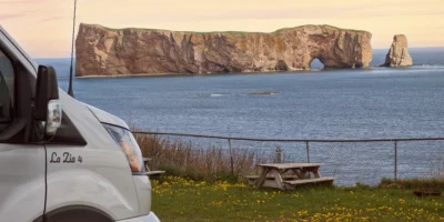 Camperbus en picknicktafel aan de kust met uitzicht op de rots van Percé in Québec