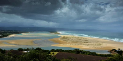 Uitzicht over de lagune, het strand en de oceaan bij Plettenberg Bay onder donkere onweerswolken