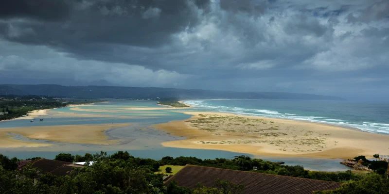 Uitzicht over de lagune, het strand en de oceaan bij Plettenberg Bay onder donkere onweerswolken