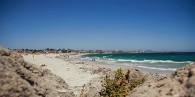 Strandbezoekers en golven bij Sorrento Beach, met rotsen op de voorgrond