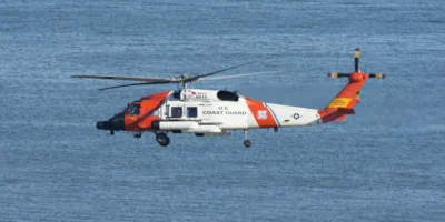 Witte en oranje helikopter van de Amerikaanse kustwacht boven een blauwe zee. Illustratieve archieffoto uit 2021; dit is geen beeld van de redding bij Ensenada in oktober 2026.